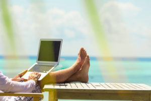 Young man with laptop and cell phone on tropical beach